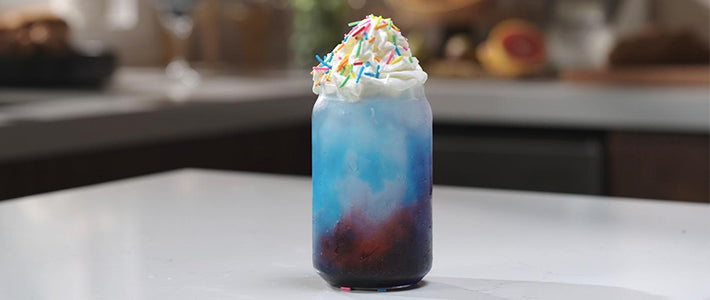 Berry Blue Whirl Slush with whipped cream and rainbow sprinkles in a glass jar on a kitchen counter.