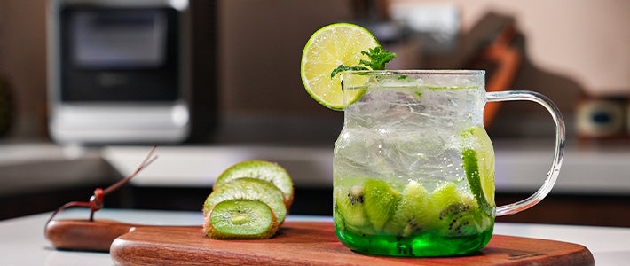 Kiwi Rum Fizz cocktail in a glass mug with ice, kiwi slices, mint, and lime garnish.
